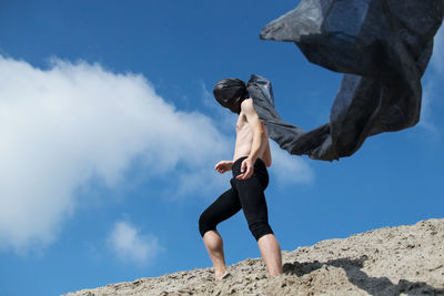 Low angle view of woman standing on rock against sky