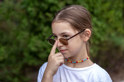 Little girl holds sunglasses with her finger and looks into the distance