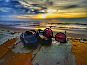 Close-up of sunglasses on sand at beach against sky during sunset