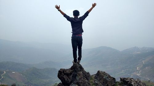 Rear view of man with arms raised against mountain range