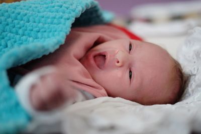 Close-up of baby girl yawning on bed at home