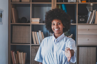 Portrait of young woman standing against shelf