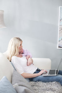 Woman holding newborn daughter and using laptop