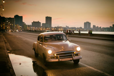 Cars on road by buildings in city at sunset