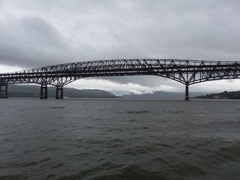 Suspension bridge over river against cloudy sky