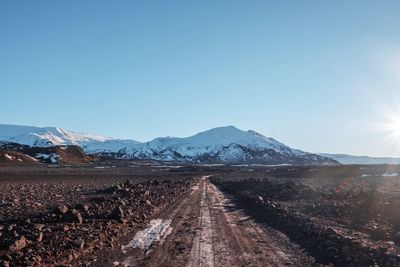 Dirt road by mountains against clear sky