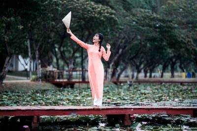 Woman with arms raised standing against trees