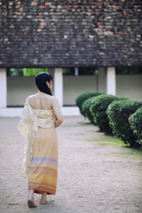 Rear view of woman standing on footpath by tree