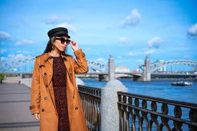 Happy young woman in light coat on the embankment posing