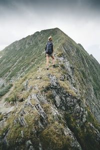 Rear view of female hiker climbing mountain against cloudy sky