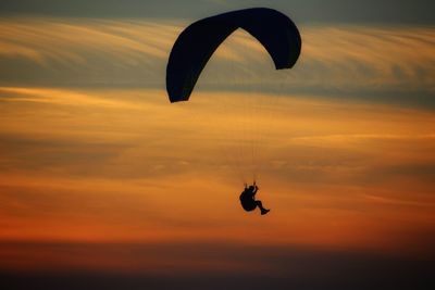 Silhouette person paragliding against sky during sunset