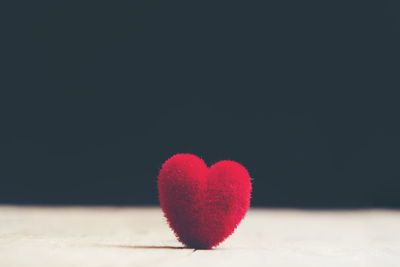 Close-up of heart shape on pink table against black background