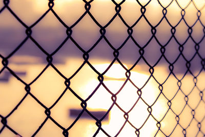 Full frame shot of chainlink fence against sky during sunset