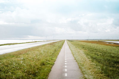 Empty road amidst field against sky