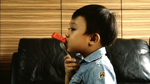 Side view of boy looking away while eating watermelon at home
