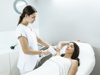 Young master doing laser hair removal procedure with professional equipment in hand in light salon