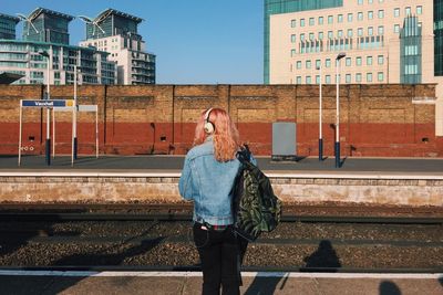 Rear view of woman with backpack standing at railroad station platform in city