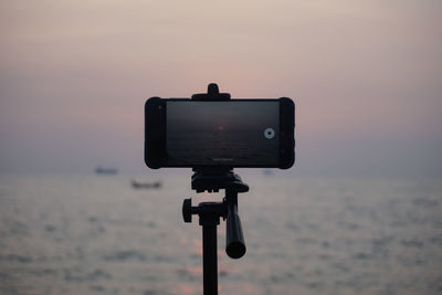 Close-up of camera on beach against sky during sunset