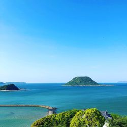 Scenic view of island on sea against clear blue sky