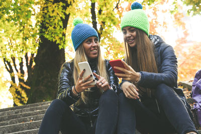 Two girls sitting in the park using smartphone. teen using mobile phone. sisters chat with friends.