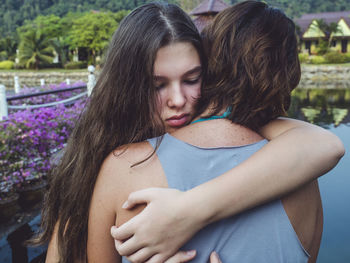 Close-up of smiling daughter embracing mother while standing outdoors