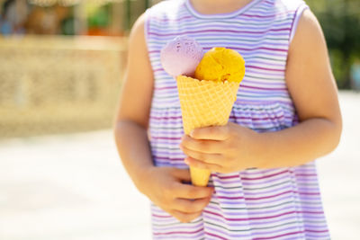 Funny blonde girl in colorful dress eating ice cream in waffle cone. summer food