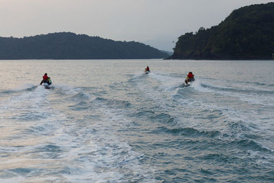 Rear view of people jet boating on sea against sky during sunset