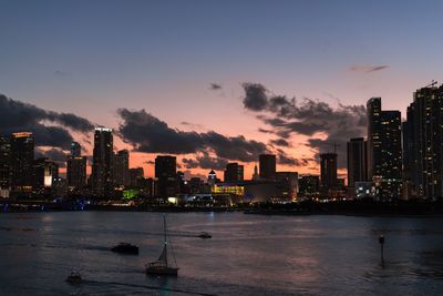 Sea by illuminated buildings against sky during sunset