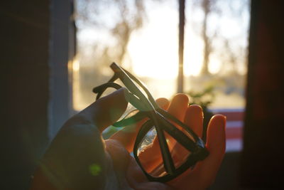 Close-up of hand holding eyeglasses at home during sunset