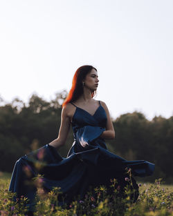 Young woman sitting in field against clear sky