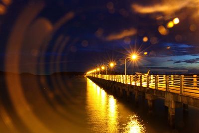 Illuminated bridge over river against sky at night