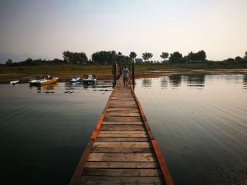 Rear view of man walking on pier over lake against sky