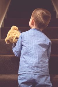 Rear view of boy carrying teddy bear upstairs