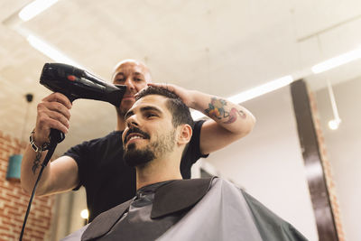 Low angle view of barber drying man hair in salon