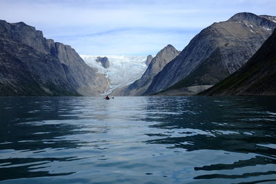 Distant person kayaking on sea against mountains