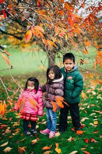Portrait of siblings standing on leaves during autumn