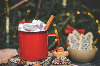 One red iron mug with hot cocoa, marshmallows on top with cinnamon, gingerbread man on cutting board