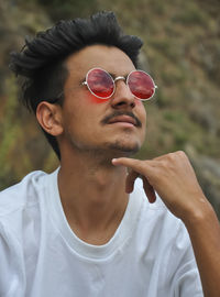 Closeup shot of a young guy posing outdoor with looking up with wearing white t-shirt red sunglasses 