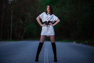 Portrait of young woman standing on road against trees