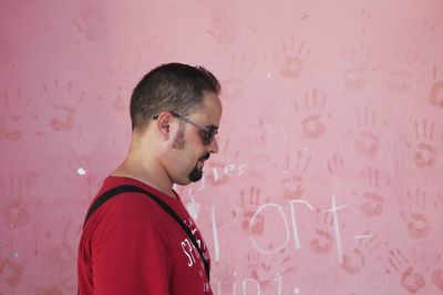 Portrait of young man standing against pink wall