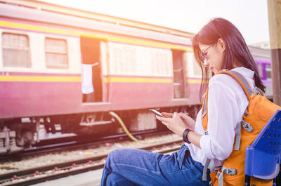 Side view of woman using mobile phone at railroad station