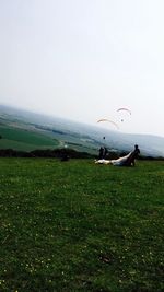 Scenic view of grassy field by sea against clear sky