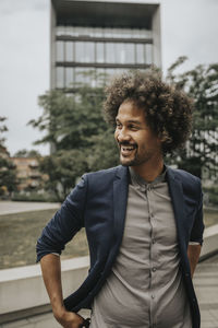 Happy man with curly hair standing in front of building