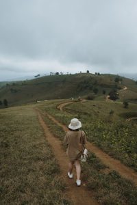 Rear view of woman walking on field against sky