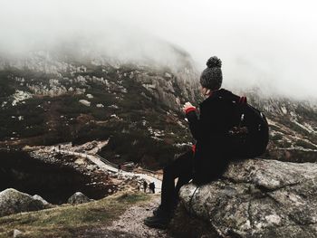 Female hiker sitting on rock by hill during foggy weather