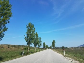 Empty road amidst trees against blue sky