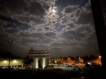 Illuminated street amidst buildings against sky at night