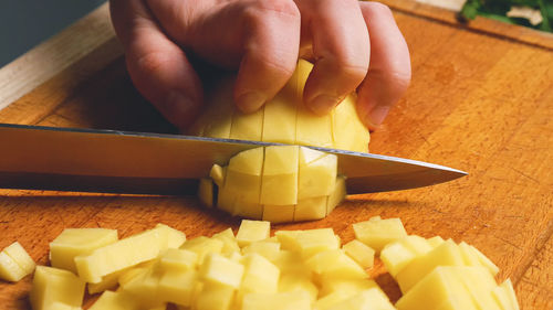 Close-up of a woman's hands with a knife slicing and dicing potatoes on a cutting board