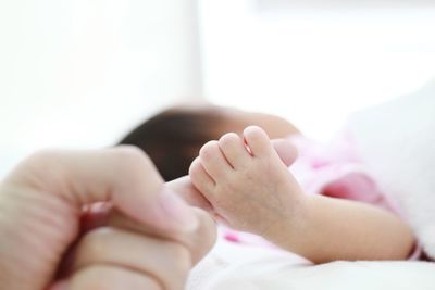 Baby holding cropped hand at home