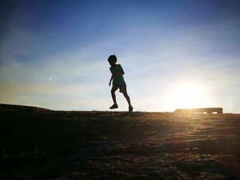 Boy standing on field against sky during sunset